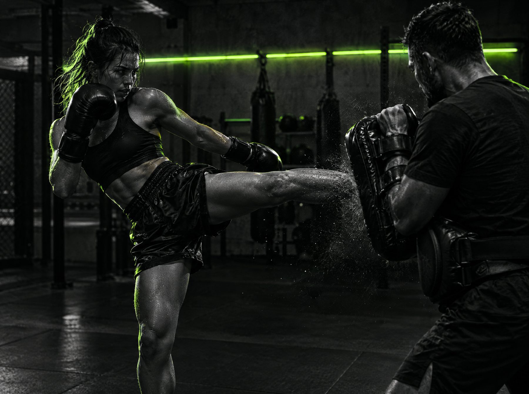 Kickboxer landing a shin kick into thai pads held by a coach