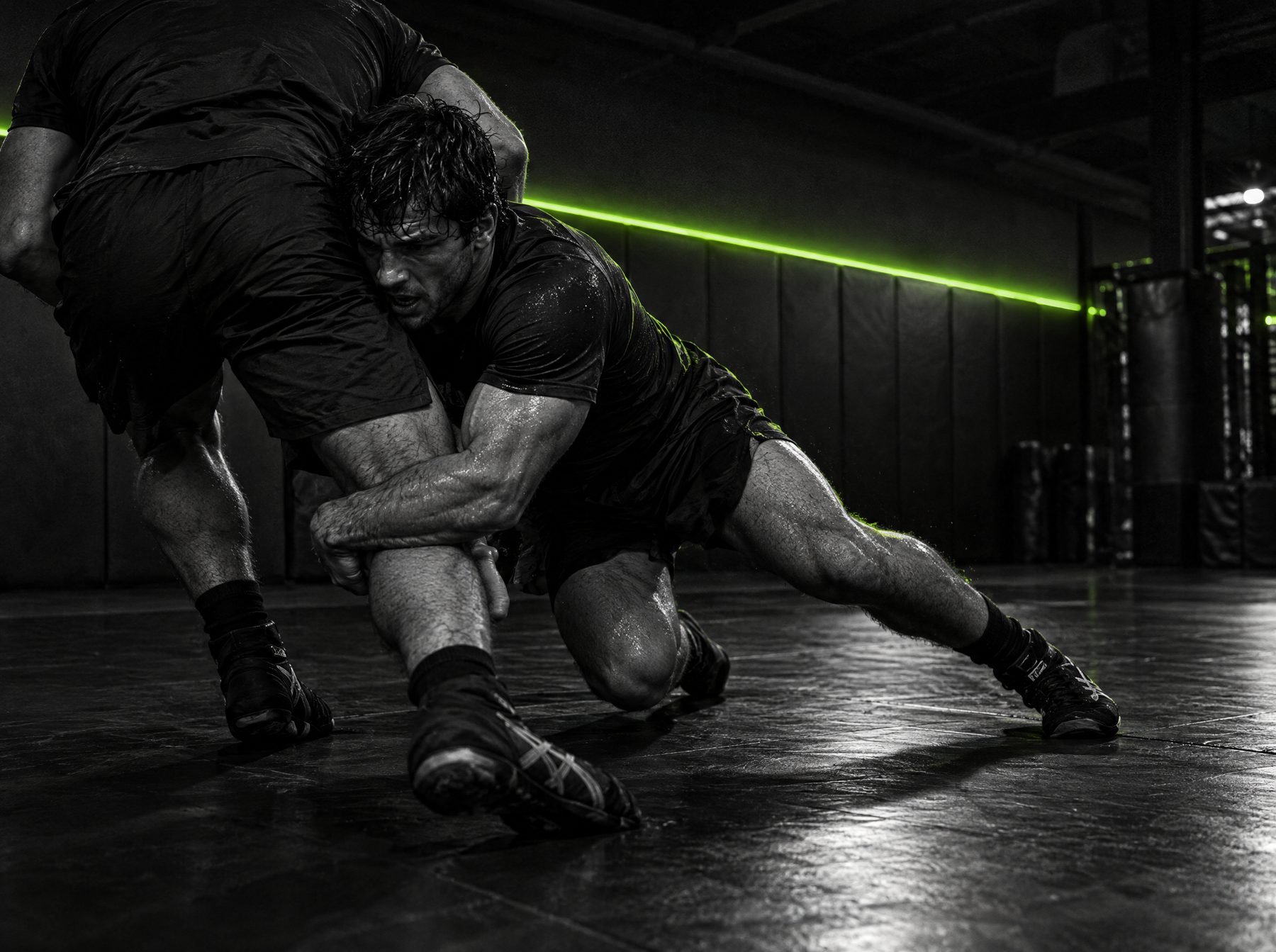 Wrestler driving through a double-leg takedown on dark training mats